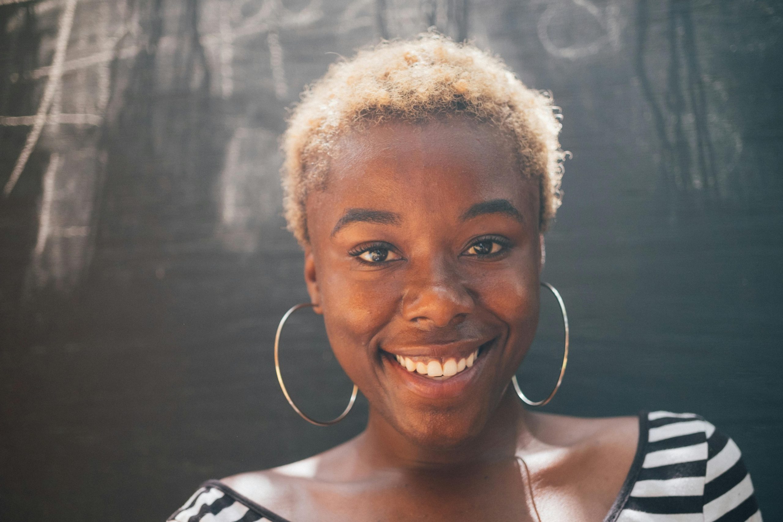 Portrait of a cheerful Black woman with afro hairstyle and hoop earrings smiling in natural light.