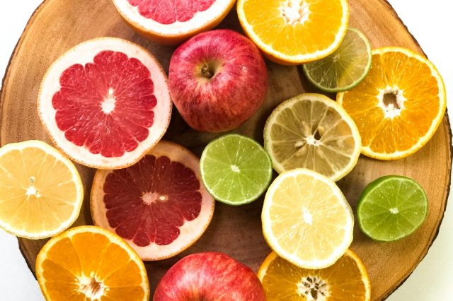 Vibrant display of sliced citrus fruits and apples on a wooden platter, emphasizing freshness and healthy eating.
